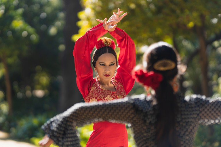 Two hispanic woman in flamenco dress and flowers on the head dancing face to face in a park in Seville